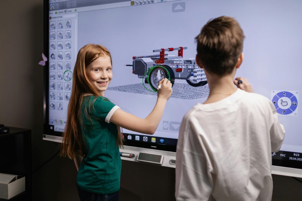 Two Kids Standing by an Interactive Board