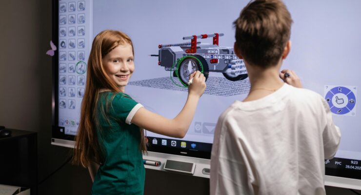 Two Kids Standing by an Interactive Board